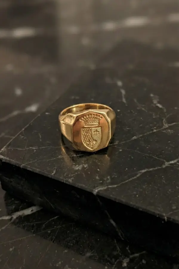 Anello chevalier scudo con stemma araldico inciso, appoggiato su una superficie di marmo nero a contrasto.